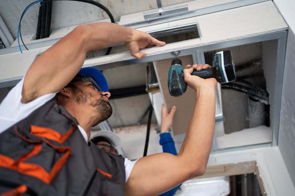 Installer using a drill to mount duct framing during an HVAC installation