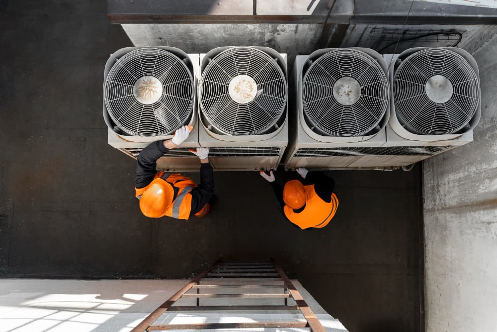 Two technicians inspecting a row of rooftop air conditioning condenser units
